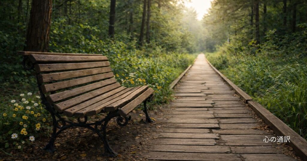 森の中に続く木の遊歩道と、板が一部ずれた古い木製ベンチ。進めるが、どこか居心地の悪さを感じる風景。